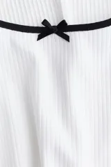 Vestido mini blanco de manga corta en punto de algodón acanalado con pollera evasé. Modelo con cuerpo entallado y escote redondo amplio con ribete fino en color negro y moña decorativa de satén. Ribete sobrehilado en mangas y bajo.