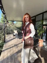 Cartera bandolera de cuero color chocolate, con forro interno de tela y flecos en la parte inferior. Tiene asa larga regulable y cierre superior con botón. Fabricada en Uruguay.