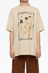 Camiseta de algodón orgánico color beige, corte oversize y manga corta ancha. Presenta un estampado central enmarcado con motivos florales y el texto "BIMBA Y LOLA" en la parte superior e inferior del diseño.