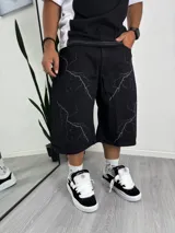 Bermuda ancha de denim negro con estampado de rayos en gris claro. Corte holgado y largo por debajo de la rodilla.