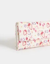 Billetera de cuerina con estampado de flores, fresas y cerezas. Tiene formato de fichero con solapa y broche en forma de corazón. Cuenta con compartimentos para tarjetas y billetes.