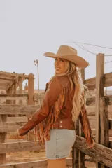 Chaqueta de cuero color marrón con corte entallado, cierre frontal asimétrico con cremallera, cuello con solapas de muesca y flecos decorativos en las mangas.