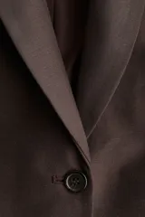 Blazer marrón de corte entallado, con solapas de pico, cierre de un botón, hombreras, bolsillos delanteros de parche, puños con abertura y botón, abertura trasera y forro interior.