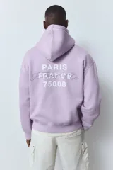 Buzo canguro lila con capucha, corte holgado, hombros caídos, bolsillo delantero y puños y bajo acanalados. Estampado con la frase "Paris, France" y "Le Triangle d'Or".