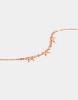 Collar corto bañado en oro rosa con cadena de eslabones y tres dijes de moño con strass rosado.