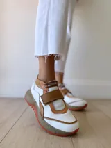 Zapatillas deportivas blancas con detalles en cuero color salmón y suela gruesa con detalles en naranja.