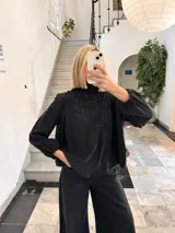 Blusa negra con cuello alto fruncido y mangas largas abullonadas con puños elásticos.