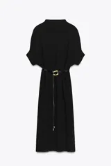 Vestido negro de tejido de punto, corte midi y silueta holgada, con cuello alto acanalado y mangas cortas tipo murciélago. Se ajusta a la cintura con un cinturón fino de efecto piel negro con hebilla dorada en forma de C.