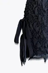 Top negro de punto con textura arrugada, cuello redondo, mangas cortas y lazos laterales.