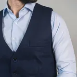 Chaleco de vestir marrón claro con textura de espiga, cuello en V, cierre frontal con botones y bolsillos ribeteados.
