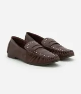 Mocasín de cuero color marrón con puntera fina, detalle de pliegues y tachuelas plateadas.