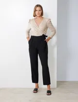 Enterito de fiesta con torso de lentejuelas color champagne, escote en V cruzado, mangas 3/4 con frunces en los hombros, cintura elastizada con lazo negro y pantalón negro de corte recto con bolsillos laterales.