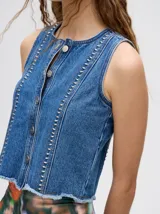 Chaleco marrón de denim con apliques metálicos y flecos en el ruedo.