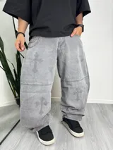 Pantalón gris de corte amplio con estampado de cruces y cadena metálica decorativa.