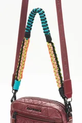 Bandolera negra de nylon matelassé con correa larga regulable y correa corta desmontable de cordones trenzados multicolores. Tiene cierre superior, bolsillo frontal con cierre, bolsillo trasero y dos bolsillos internos.