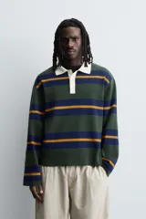 Polo de punto de corte relajado con diseño de rayas horizontales en tonos verde, azul y mostaza. Presenta cuello solapa en color crema a contraste y cierre frontal con tres botones.