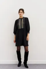 Minivestido negro de viscosa con corte en la cintura, detalles de puntillas en cuello y ruedo, gota en la espalda y pechera bordada en hilo con apliques.