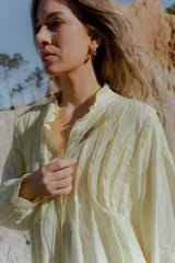 Camisa amarilla de algodón, corte suelto y largo asimétrico, más larga atrás que adelante. Tiene mangas largas amplias.