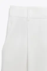 Pantalón negro de tiro alto con trabillas, pinzas delanteras, bolsillos laterales y falsos bolsillos de vivo en la espalda. Cierre frontal con cremallera y botón.