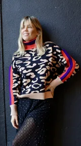 Sweater de punto con cuello alto, puños y ruedo acanalados color beige. Presenta un estampado animal print en tonos beige sobre fondo negro. Las mangas largas tienen rayas verticales en color naranja y violeta.