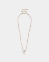 Collar corto de mostacillas color rosa pálido con dije de corazón blanco con detalle de strass y cadena dorada ajustable.