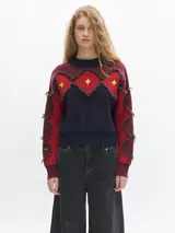 Sweater de lana color borgoña con cuello redondo y apliques de rombos rojos con flecos marrones y estrellas amarillas en el frente y los brazos.