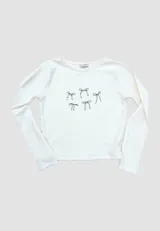 Remera blanca de algodón, estilo baby tee, con mangas largas y estampado de moños negros.