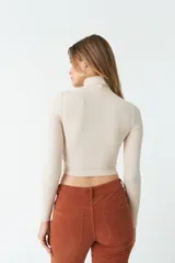 Polera color beige de corte crop, cuello alto y mangas largas.