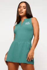 Vestido deportivo color verde con logo bordado en blanco en el pecho. Diseño sin mangas, con cuello mao y cierre parcial con botones. Falda con corte evasé y short interno.