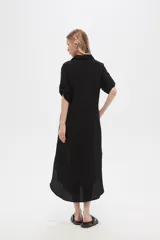 Vestido camisero midi negro de corte holgado, con cuello camisero, mangas cortas con trabillas, cierre frontal con botones, bolsillo en el pecho y bolsillos laterales.