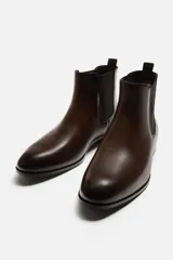 Bota Chelsea de cuero color marrón oscuro, con puntera fina, paneles laterales elásticos y tirador trasero.