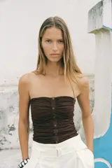 Top bustier marrón de lino con escote recto, hombros descubiertos, detalle de frunces, falsos botones delanteros y nido de abeja elástico en la espalda.