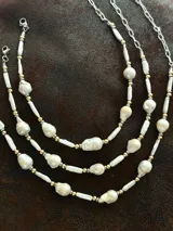 Collar corto de perlas de río alargadas y ovaladas, con cuentas de acero quirúrgico y bolitas con baño de oro. Cierre con cadena de acero quirúrgico y gancho para regular el largo.