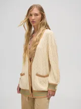 Cardigan largo color crema con detalles en color camel en el borde de los bolsillos, en el borde de los botones y en los puños. Tiene cuello en V y cierre con botones.