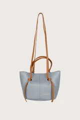 Bolso pequeño de cuero sintético color celeste con textura granulada. Tiene doble asa corta y correa larga ajustable color marrón.
