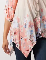 Blusa de gasa color beige con estampado floral en tonos rosa y celeste. Tiene cuello a la base, escote en V y abertura central con botones. Las mangas son 3/4 y regulables con presilla y botón.