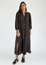 Vestido largo color beige de lino, con mangas largas abullonadas y volantes verticales en el frente. Cierre frontal con botones.