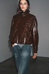 Chaqueta de Zara Woman Collection en tejido con acabado brillante efecto cuero. Presenta cuello solapa, manga larga con trabillas ajustables, bolsillos delanteros y cierre frontal con botones ocultos bajo solapa.