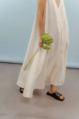 Vestido largo confeccionado en lino de color beige, con escote en V, diseño sin mangas y silueta holgada de caída fluida.