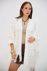 Poncho color crudo de tejido calado con diseño de rombos y flecos en el borde inferior.