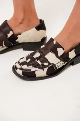 Mocasín de cuero con estampado animal print de vaca en tonos marrón y blanco, con capellada enrejillada y suela plana con plataforma delantera y taco bajo.
