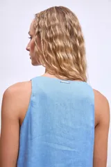 Vestido corto sin mangas, color celeste claro, con escote en V y un pequeño broche decorativo en la abertura frontal. Presenta un corte holgado tipo babydoll con bolsillos laterales y un ruedo con volado.