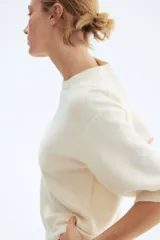 Remera de punto color crema, de corte holgado con hombros caídos y mangas cortas al codo. Presenta cuello redondo y remates acanalados en cuello, puños y bajo.