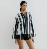 Camisa blanca con rayas verticales negras, de manga larga y corte recto. Tiene cuello clásico, cierre con botones y bolsillo en el pecho.