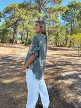 Camisa de algodón color verde militar con estampado floral en tonos claros. Presenta cuello camisero, botones frontales y mangas largas que se pueden remangar.