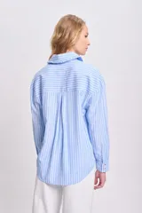 Camisa celeste a rayas verticales blancas, de manga larga con puños elásticos y volados en el frente.