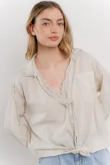 Camisa color crema de manga larga con cuello camisero y detalles de encaje en el escote. Se ata en la parte delantera.