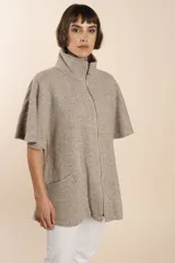 Capa acampanada color beige con manga corta, cierre metálico a la vista, cuello recto, bolsillos con tapa y terminaciones envivadas. Confeccionada en lana fina sin teñir, diseñada exclusivamente por Don Baez.