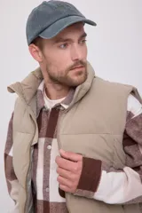Chaleco acolchado sin mangas color beige, con cuello alto y cierre de cremallera.