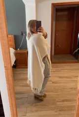 Ruana color crema con flecos en el borde.